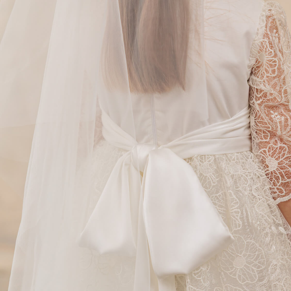 Close-up of a white lace dress with a bow detail on a neutral background