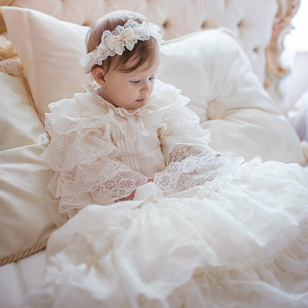 Baby in a lace dress sitting on a plush white cushion