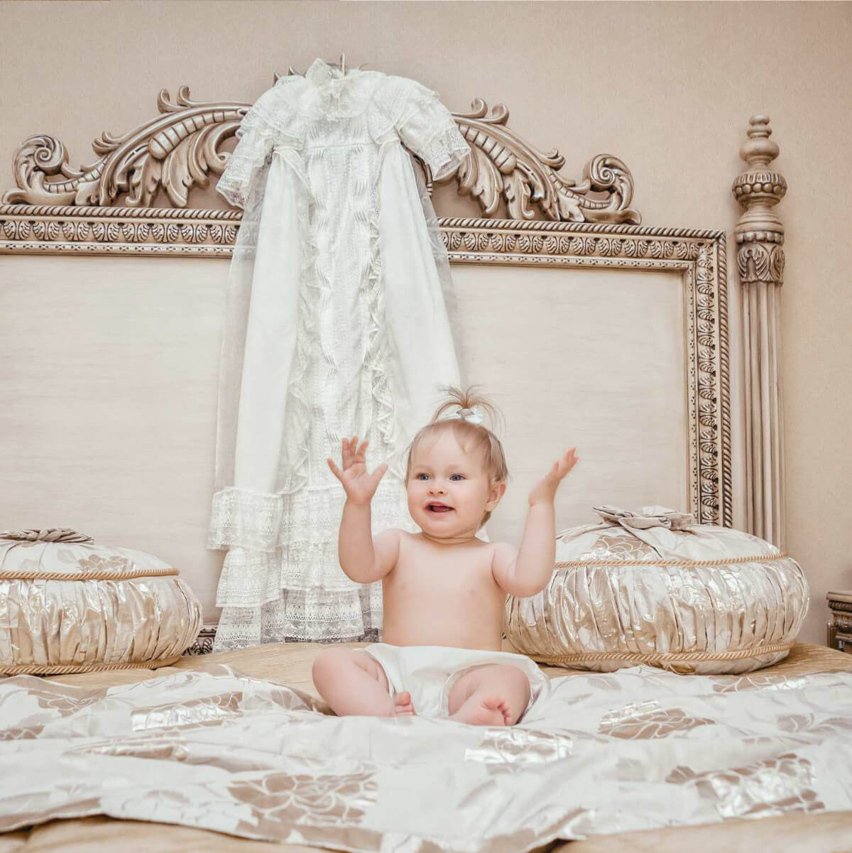 Baby sitting on a bed with decorative headboard and pillows