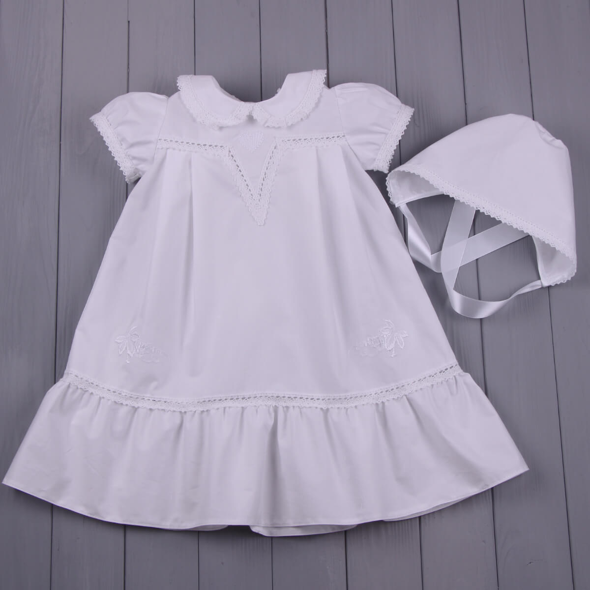Baptism Gown Set with Hat for Girl with ruffled collar and hem on a gray wooden surface