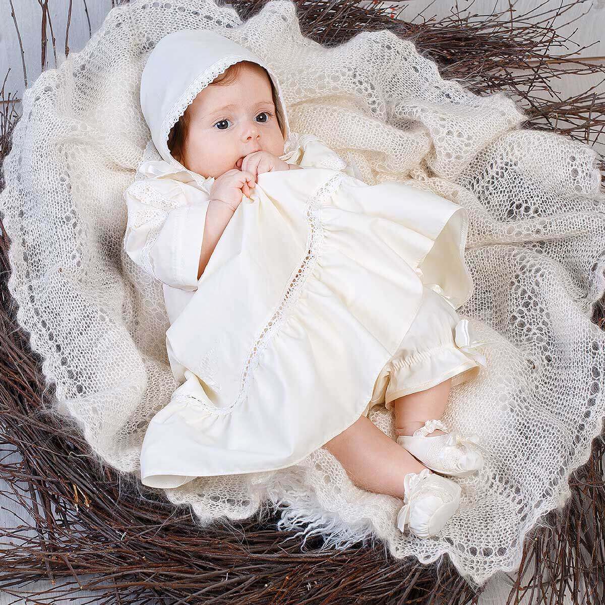 Baby wrapped in Girls Baptism Gown sitting in a nest with lace and branches.
