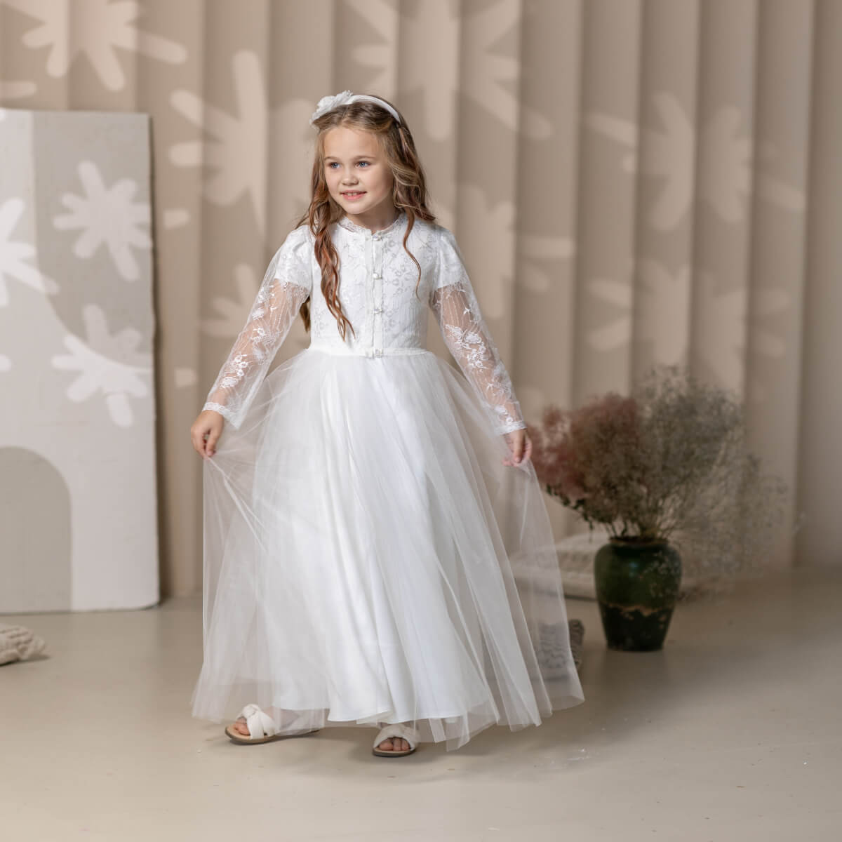 Young girl in a white lace Catholic Communion Dress standing indoors with a neutral background