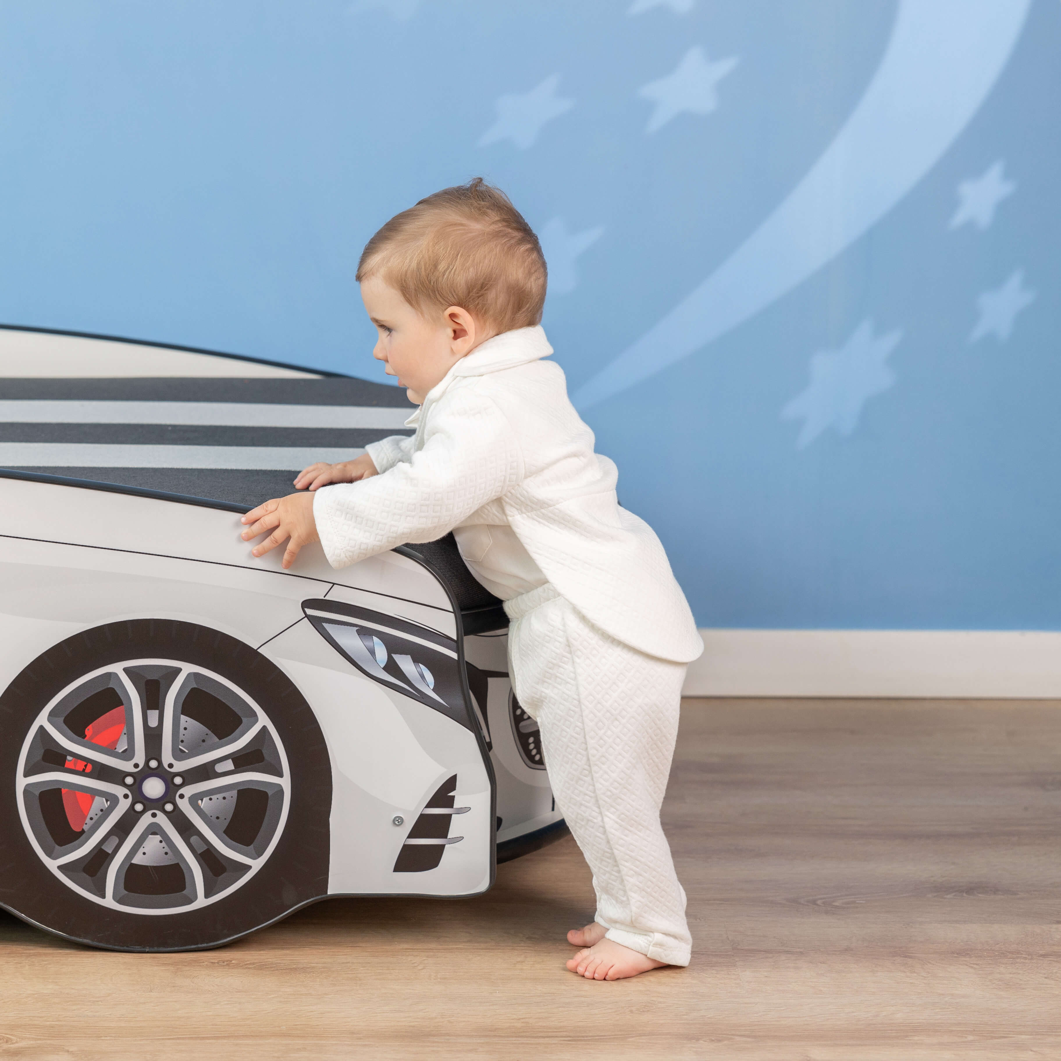 Child in a Baby Boy Baptism Suit – standing next to a toy car against a blue wall with star patterns.