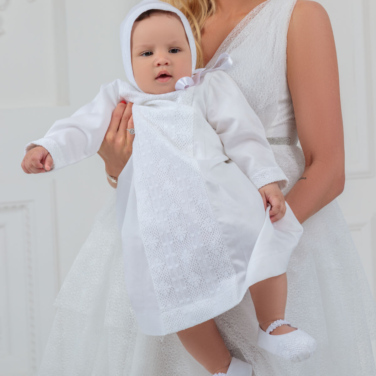 Baby in a Baptism Gown for Boy with a hood, standing next to a person in a white dress.
