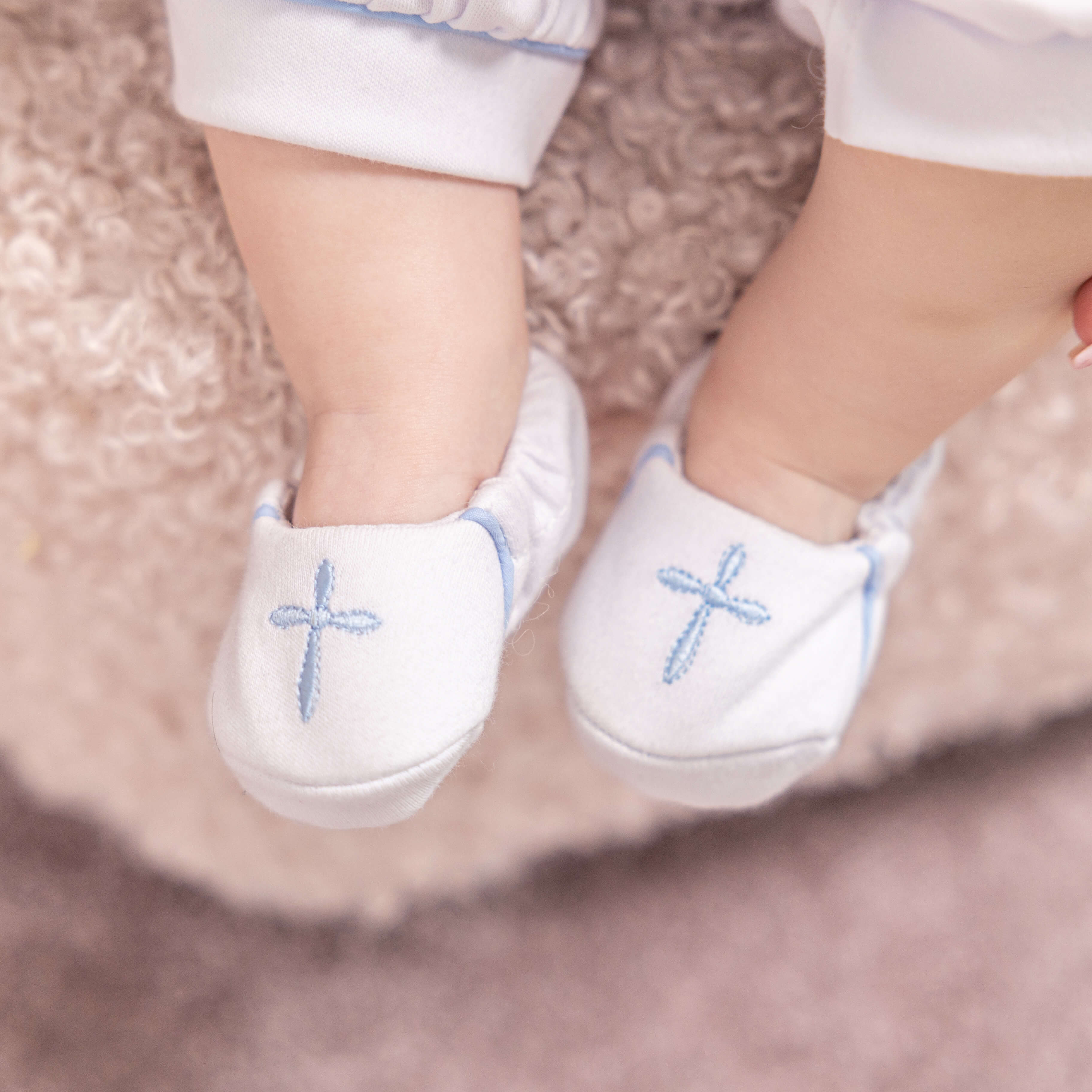 White baby shoes with blue cross designs is a part of Baptism Outfit for Boys on a soft surface