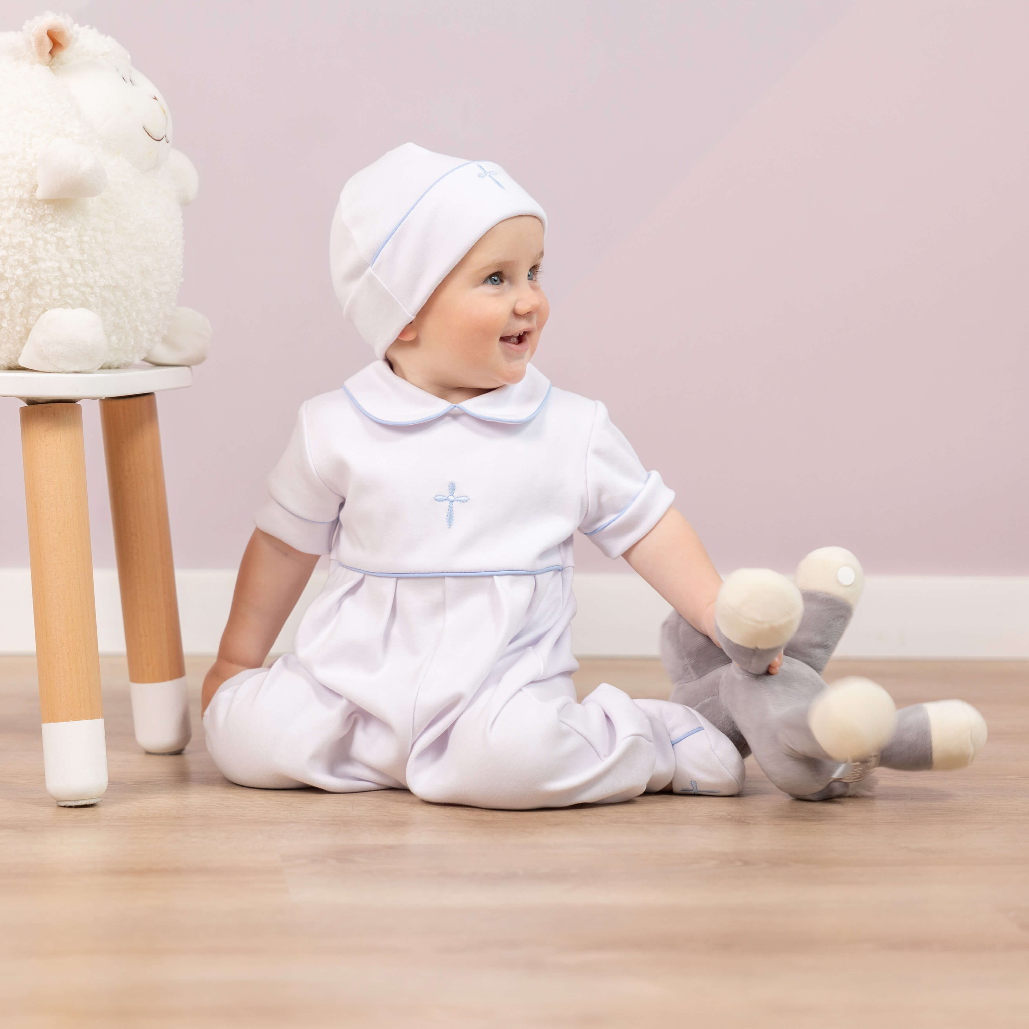 Baby in a Baptism Outfit for Boyst with a cross, sitting on the floor with toys.