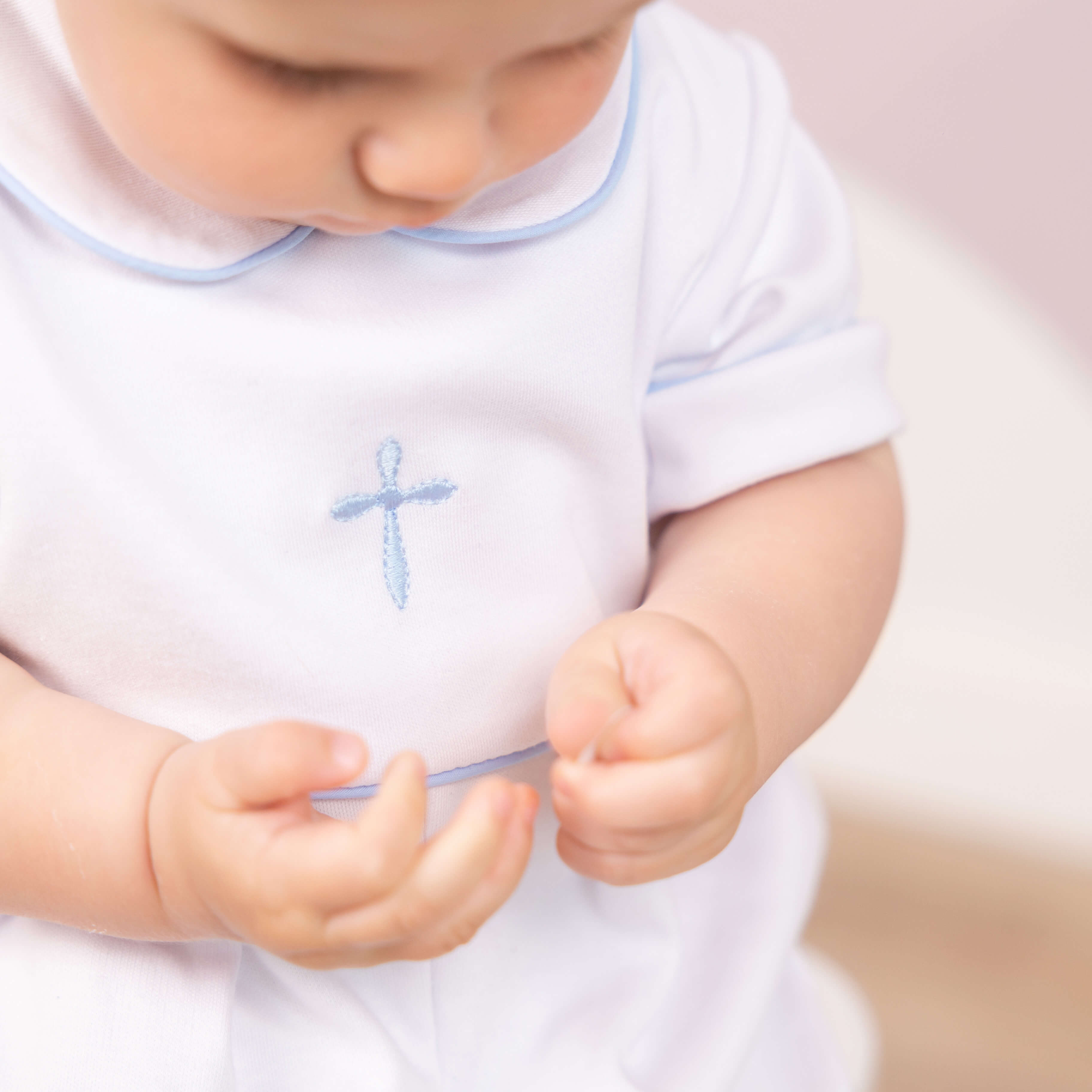 Baby in a Baptism Outfit for Boys with a blue cross holding a small object.
