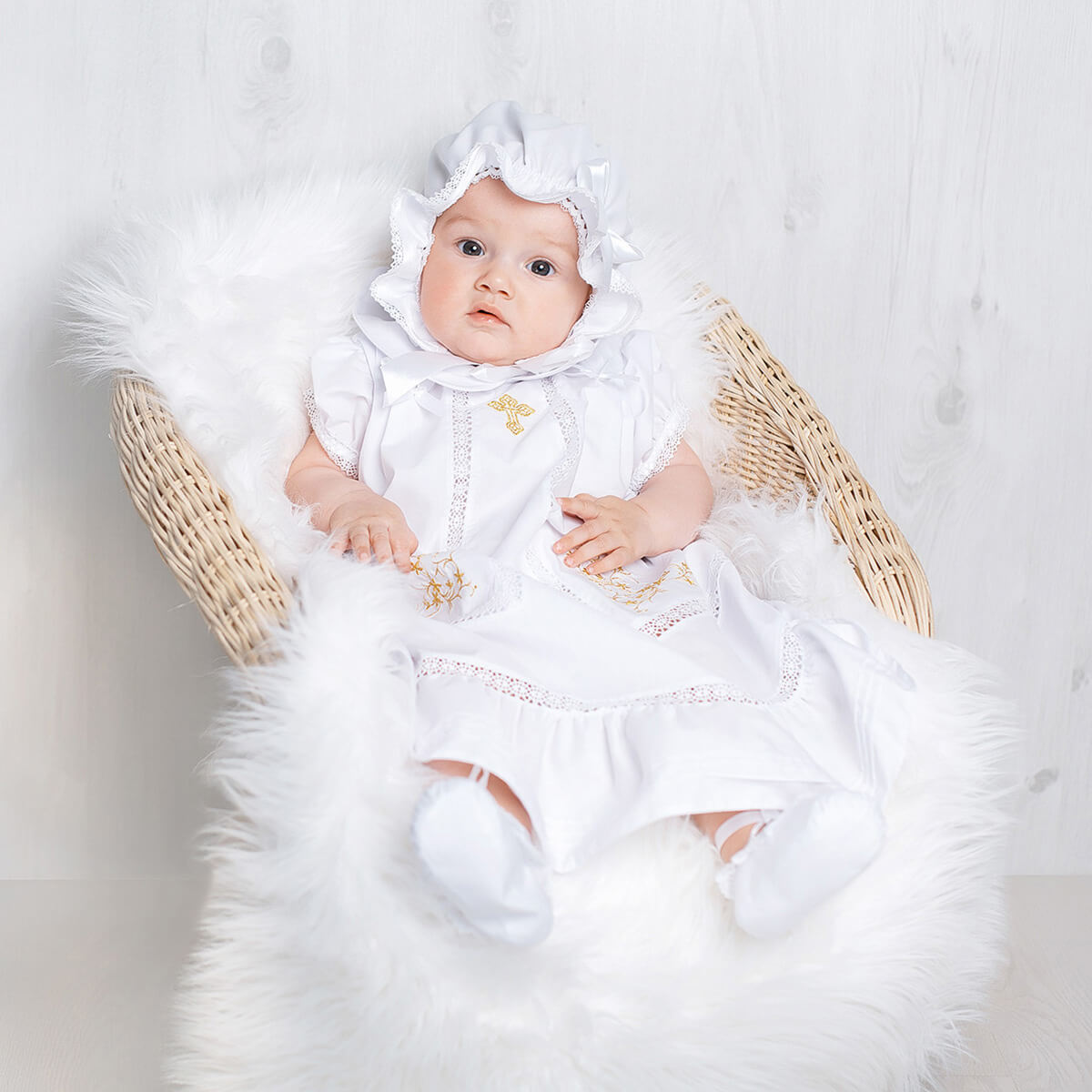 Baby in a White Christening Dress with a hood, sitting on a fluffy white surface.