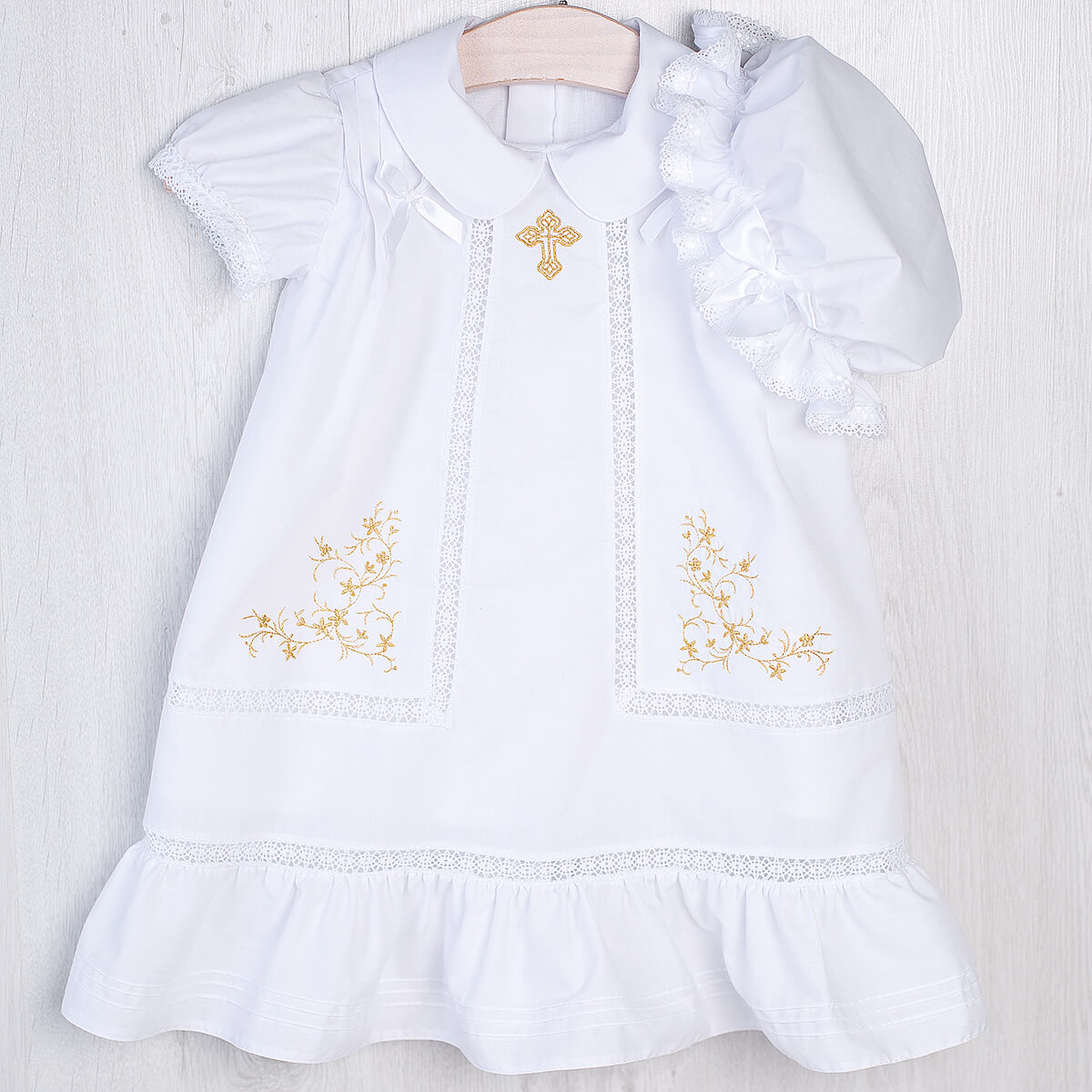 White Christening Dress with gold embroidery on a wooden surface