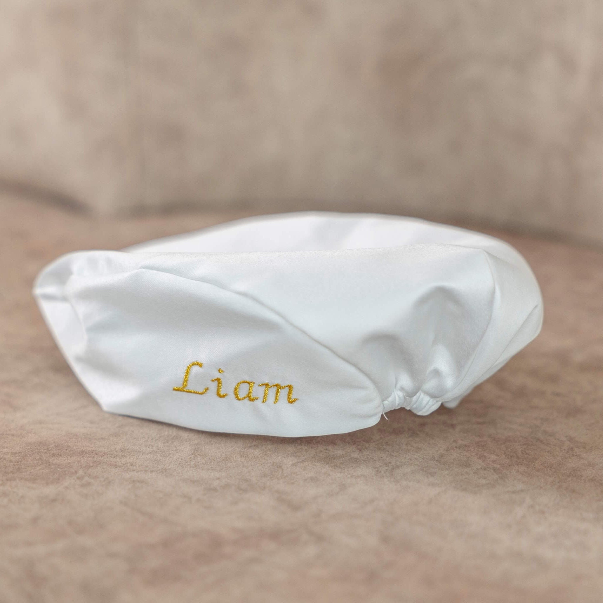 Boy Christening Hat with 'Liam' embroidered on it, placed on a soft surface.