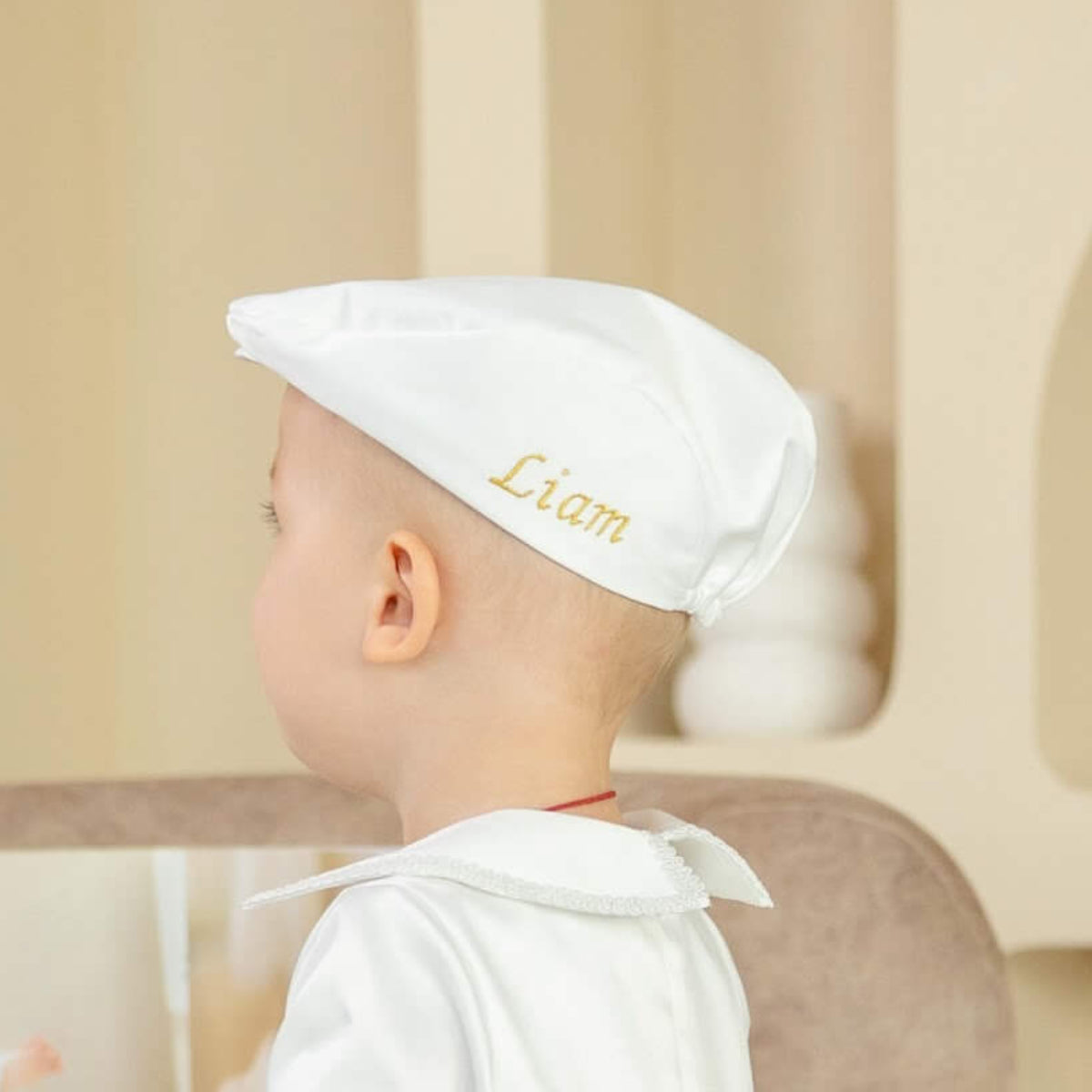 Baby wearing a Boy Christening Hat with 'Liam' embroidered on it, sitting in a high chair.