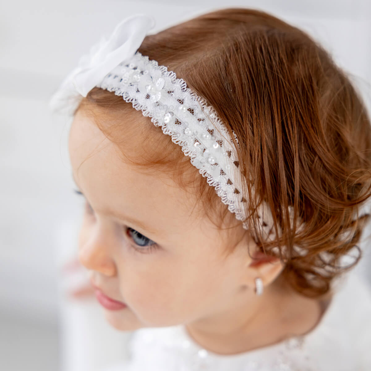 Girl wearing baby headband with a bow on a plain background