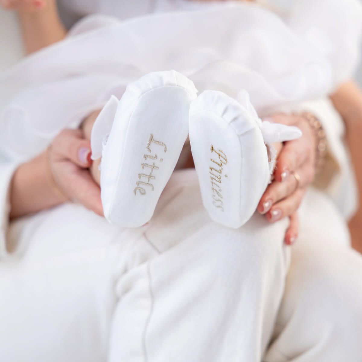 Christening Booties with 'Little' and 'Girl' text held by a person in a white robe.
