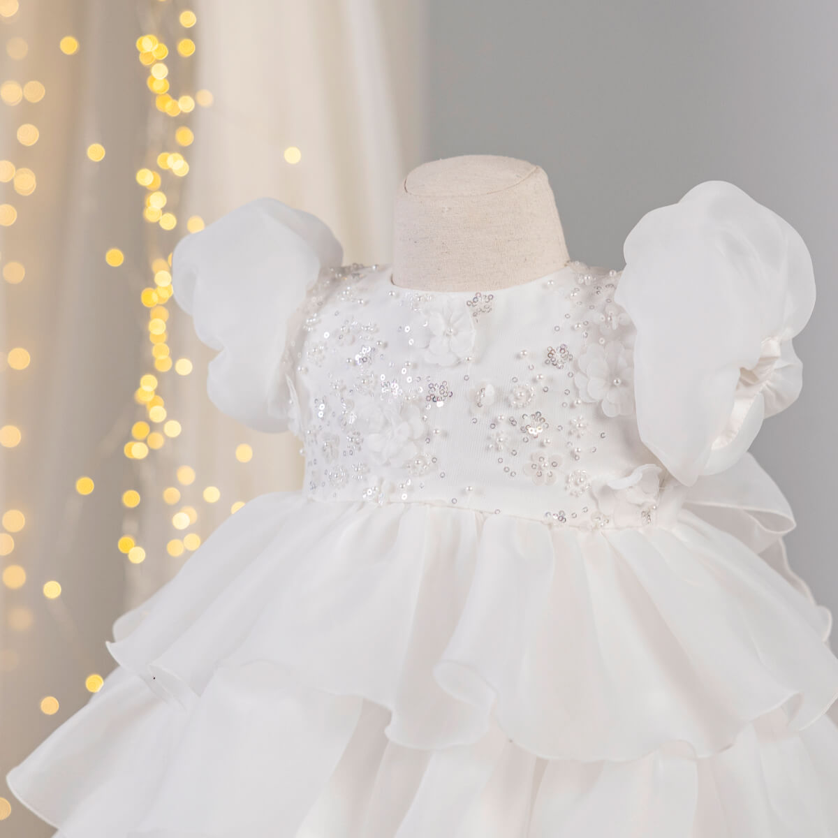 Baptism Dress with Detachable Train with ruffled sleeves on a mannequin against a soft, blurred background.