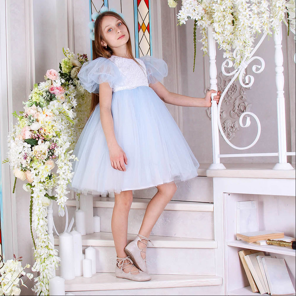 Young girl in a light blue dress standing in a decorated room with flowers and stained glass.