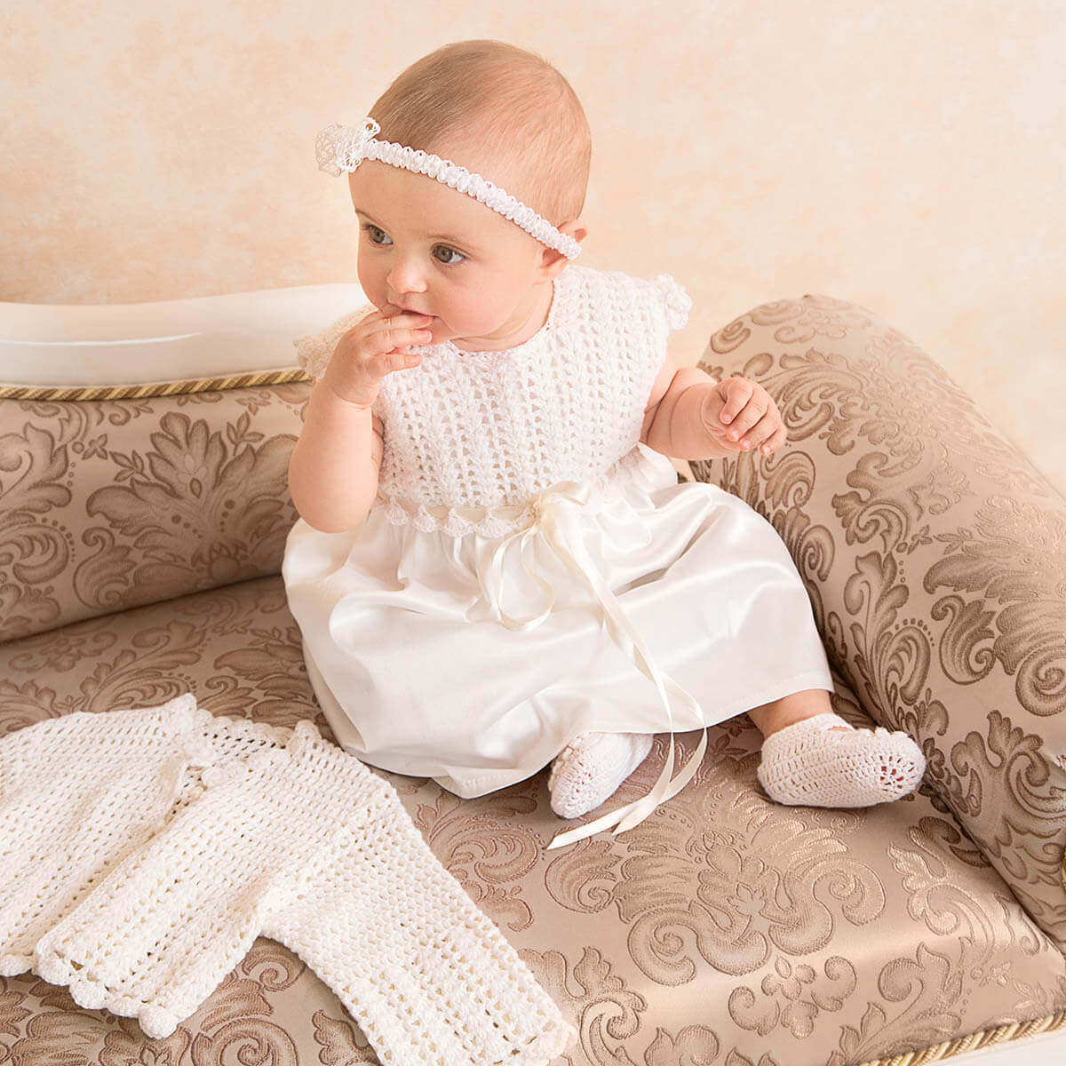 Baby in a Crochet Christening Dress sitting on an ornate couch