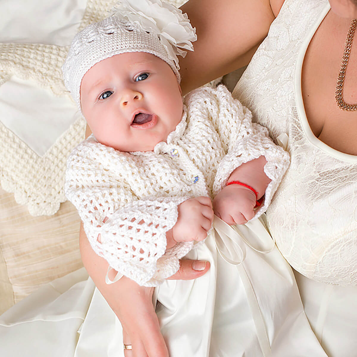 Baby in crochet baptism bonnet held by a person in a white dress.