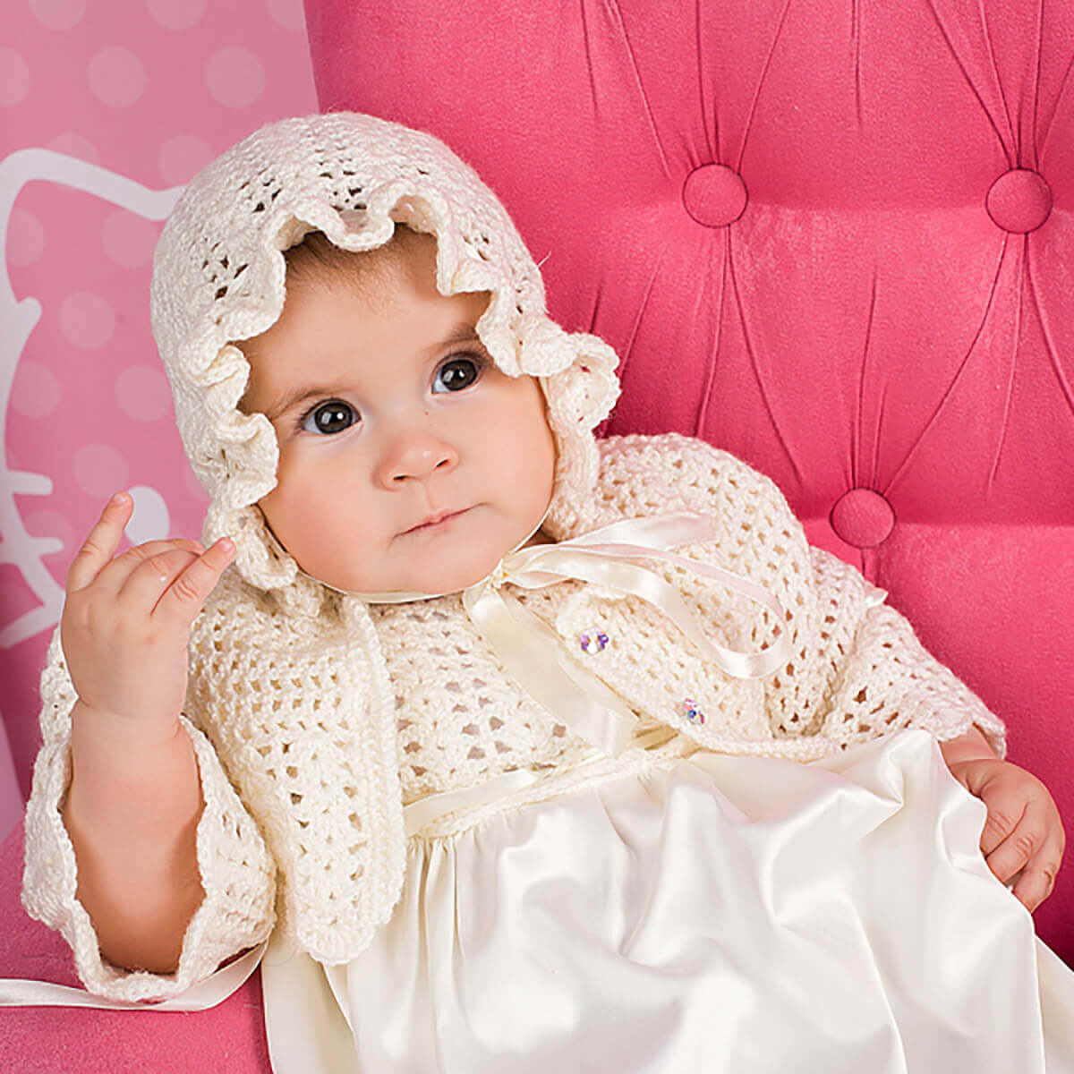 Baby wearing a Crochet Christening Bonnet and dress against a pink background