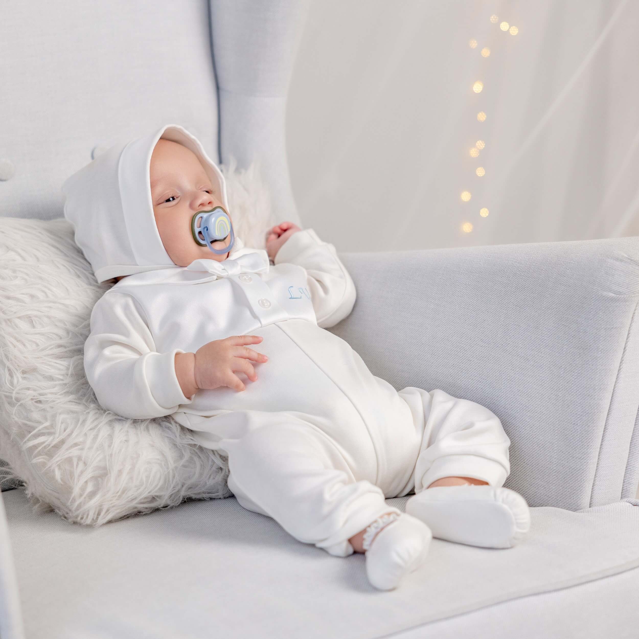 Baby in a Coming Home Romper with a hood sitting on a couch.
