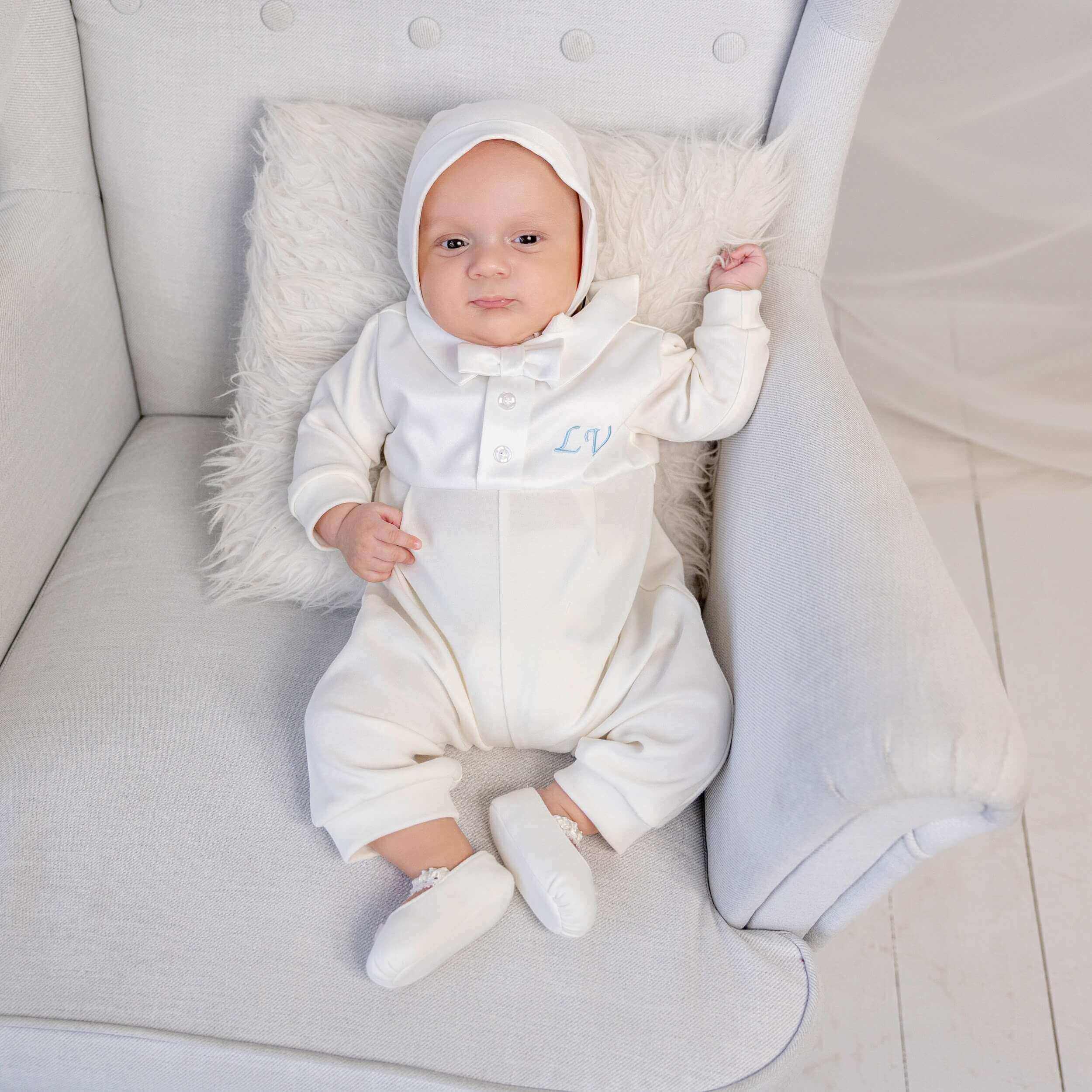 Baby in a Coming Home Romper with a hood sitting on a light gray couch.