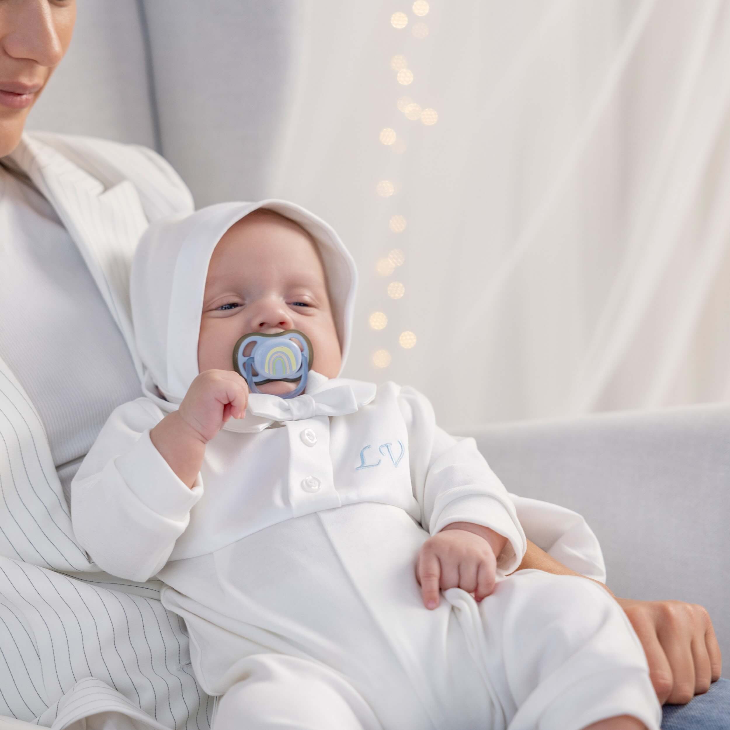 Baby in a Coming Home Romper ith a pacifier, held by a person in a soft, indoor setting.