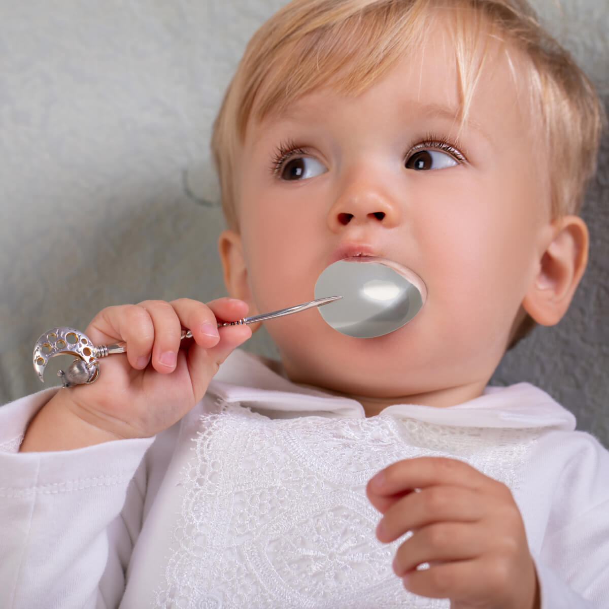 Baby with a spoon and a pacifier in its mouth against a neutral background