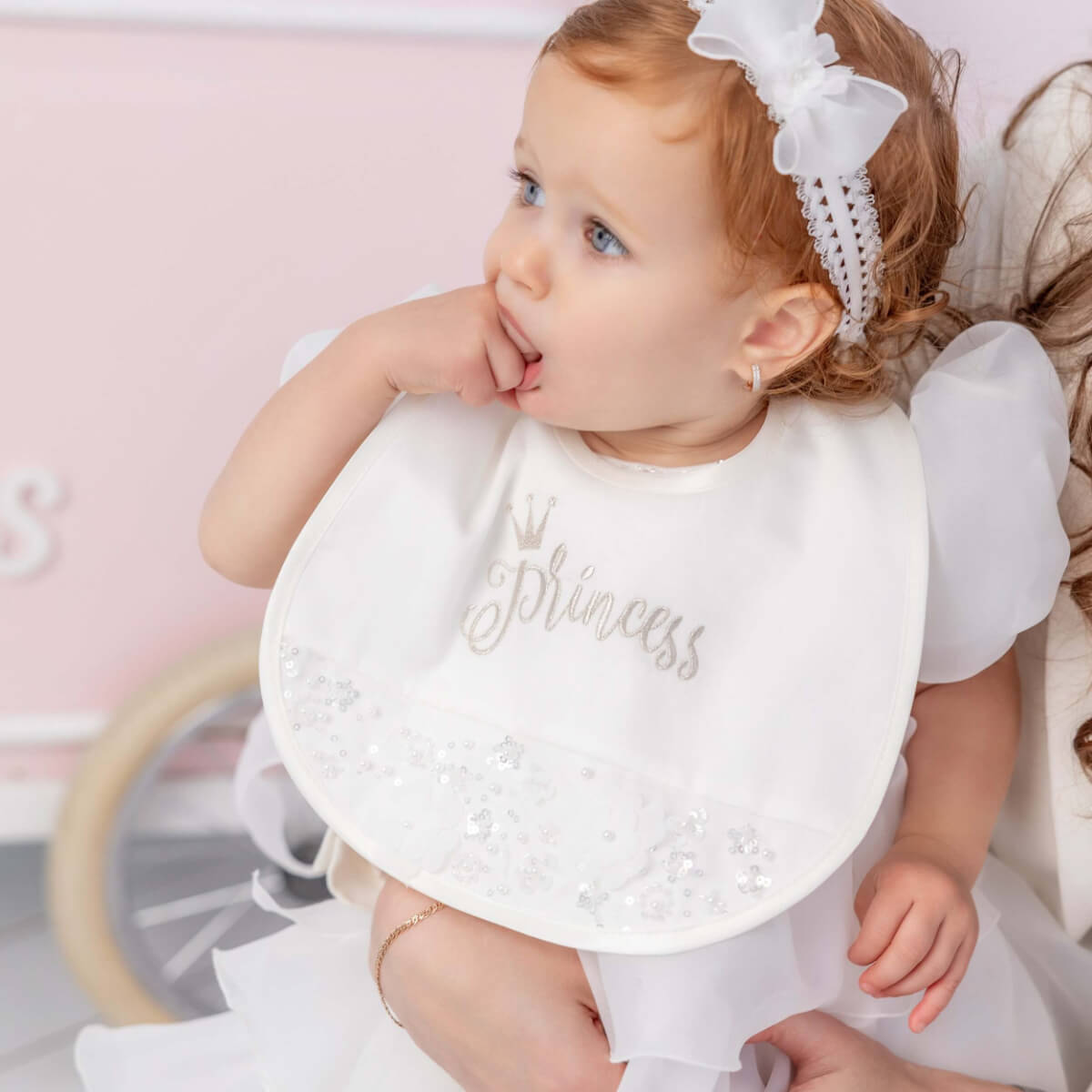 Baby wearing a white bib with 'Princess' printed on it, sitting in a crib.