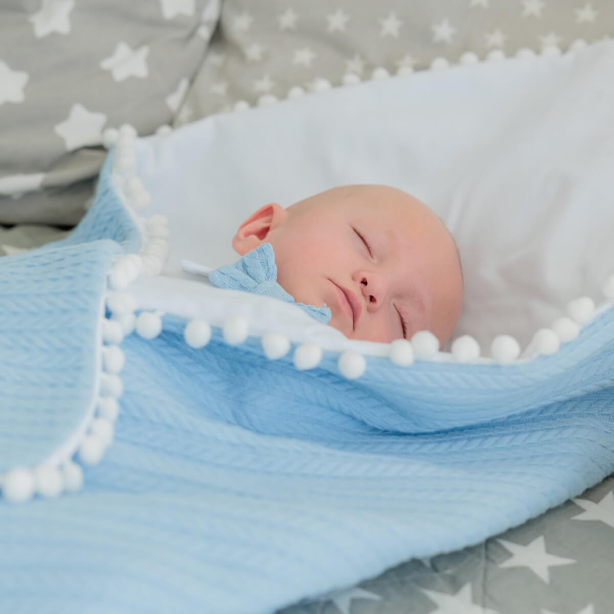 Newborn baby sleeping under a Coming Home Blanket with white stars on a gray blanket