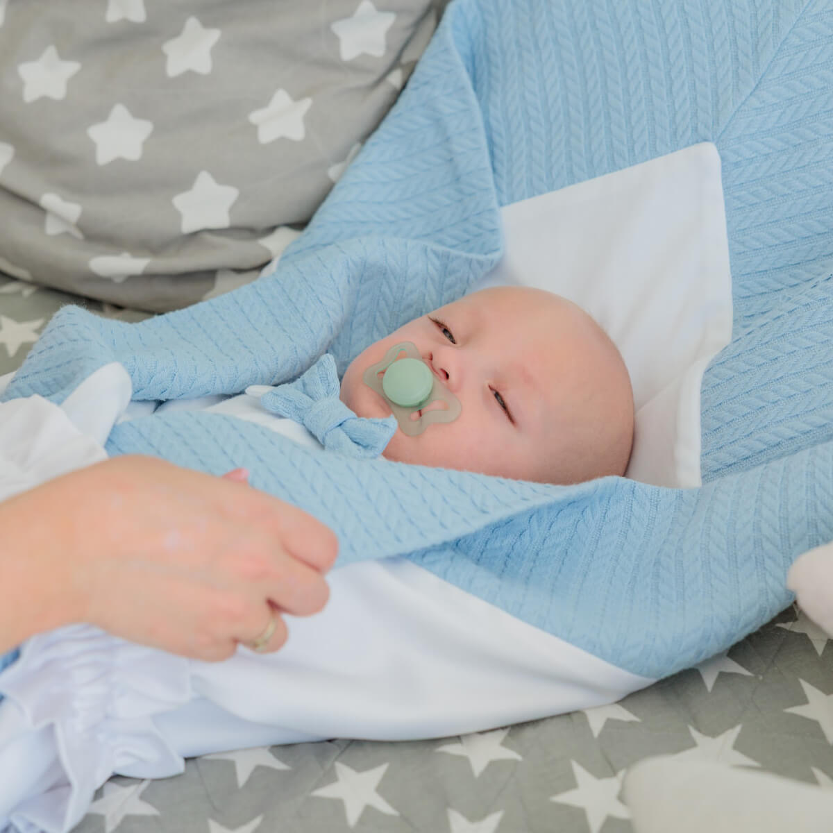 Coming Home Blanket with a pacifier, lying on a gray blanket with white stars.