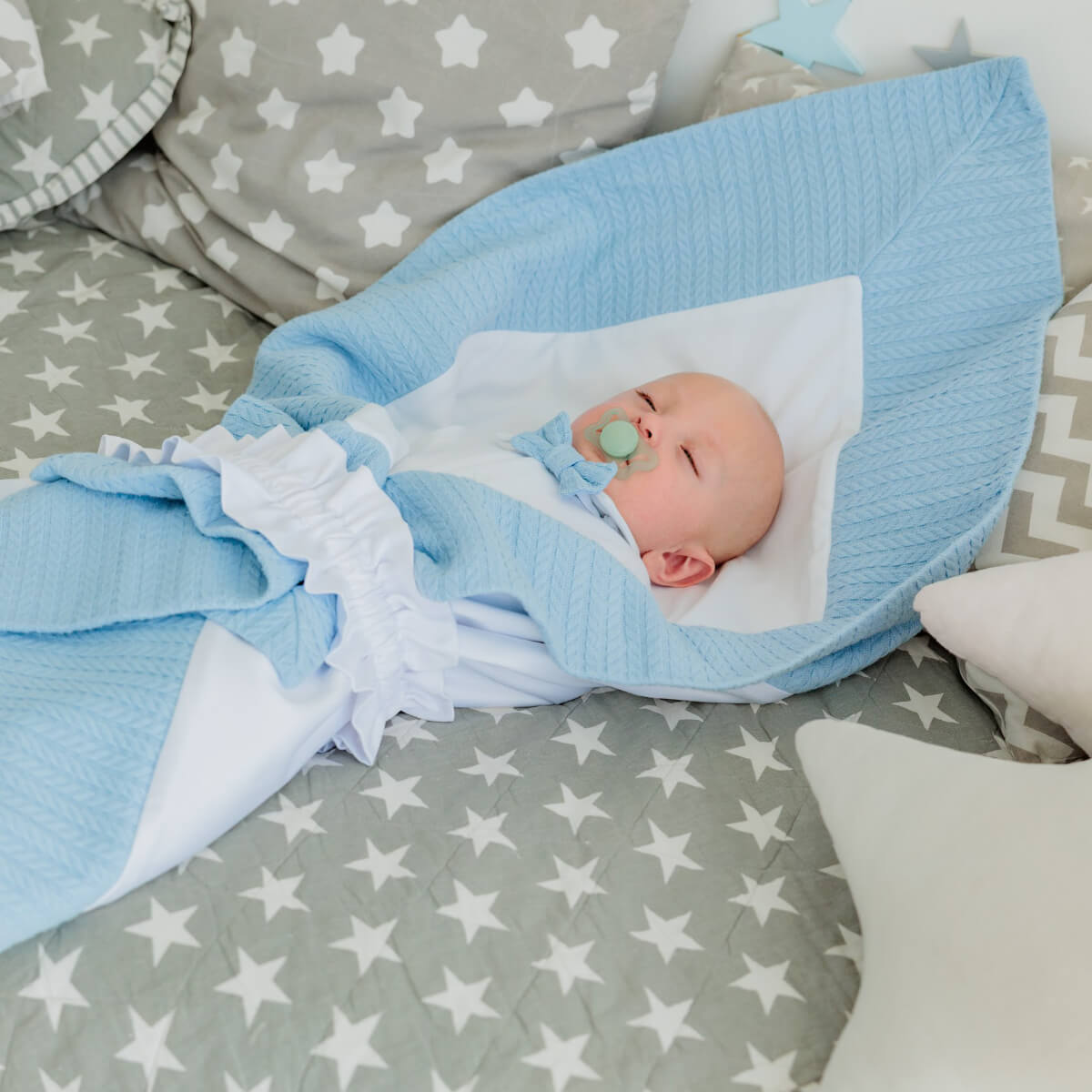 Newborn baby wrapped in Coming Home Blanket on a star-patterned blanket