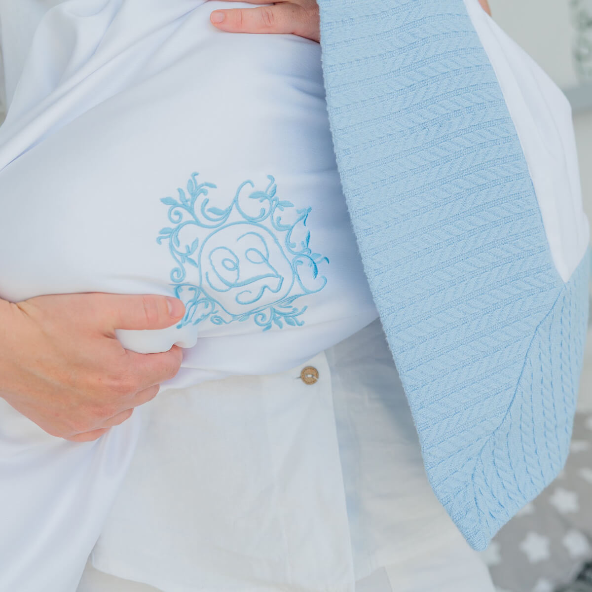 Coming Home Blanket on a white garment with a hand holding it.