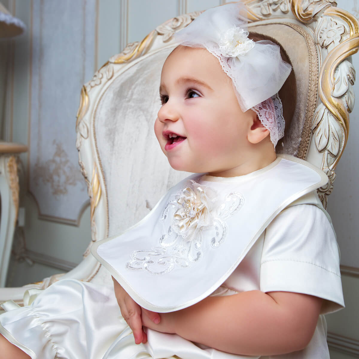 Baby in formal attire with sitting on an ornate chair.