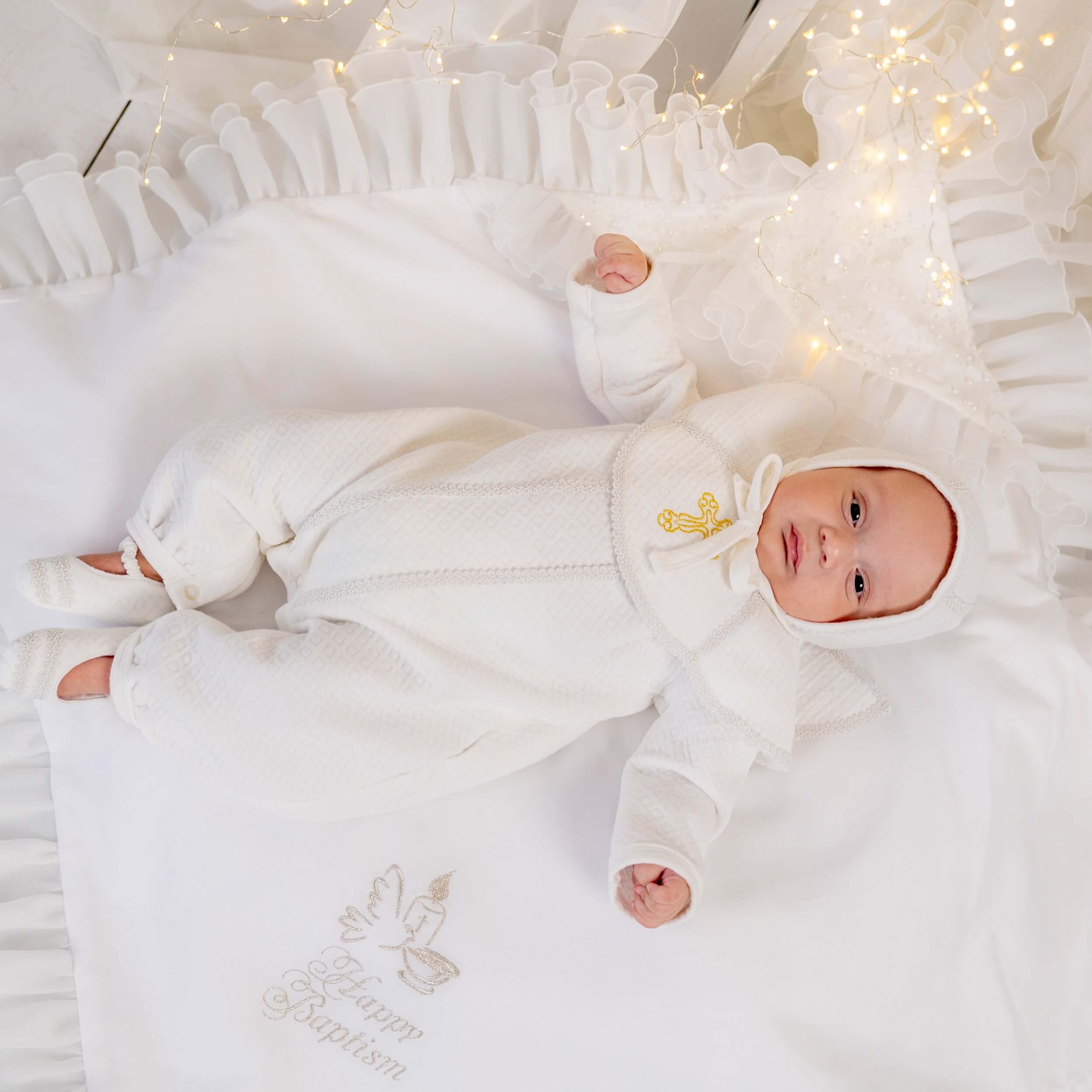 Baby in Baptism Outfit for Boys lying on a white blanket with decorative elements