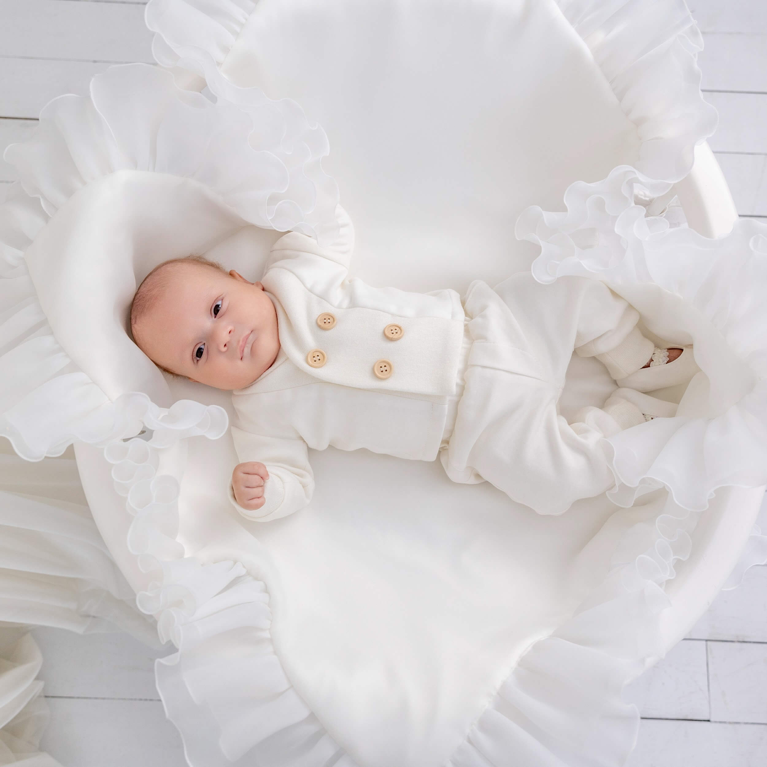 Baby in a baptism outfit for boys lying on a white textured surface