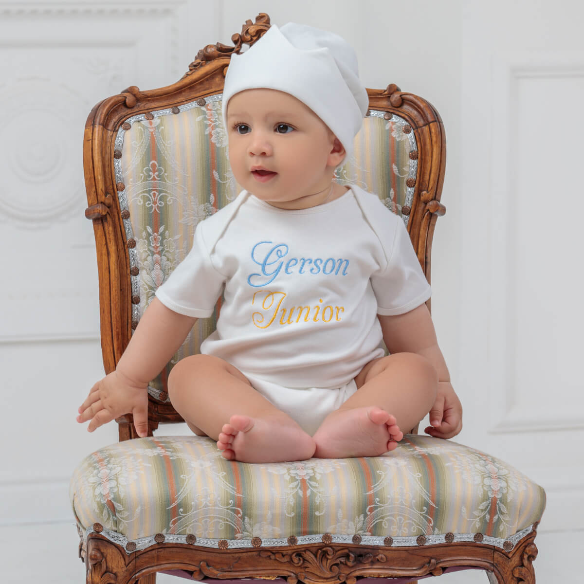 Baby sitting on a decorative chair wearing a Coming Home Bodysui with text