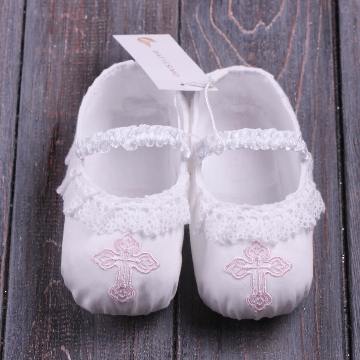 Personalized Baby Keepsake Booties with lace details and cross embroidery on a wooden surface