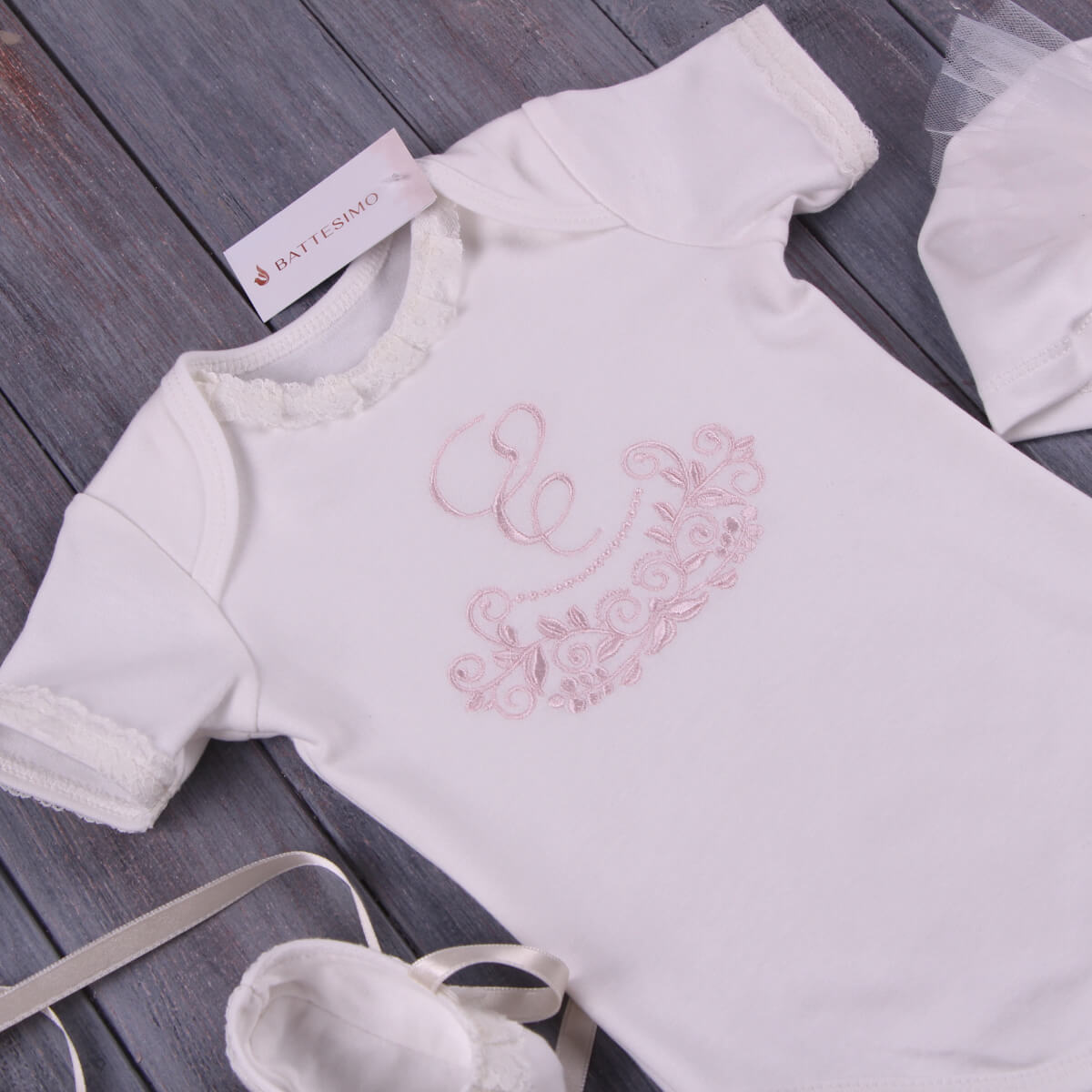 Coming Home Bodysuit with pink embroidery on a wooden surface, featuring a brand tag.