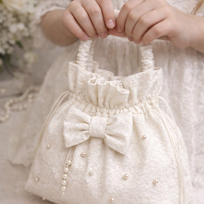 White handbag with a bow and pearl details held by a person in a textured dress.