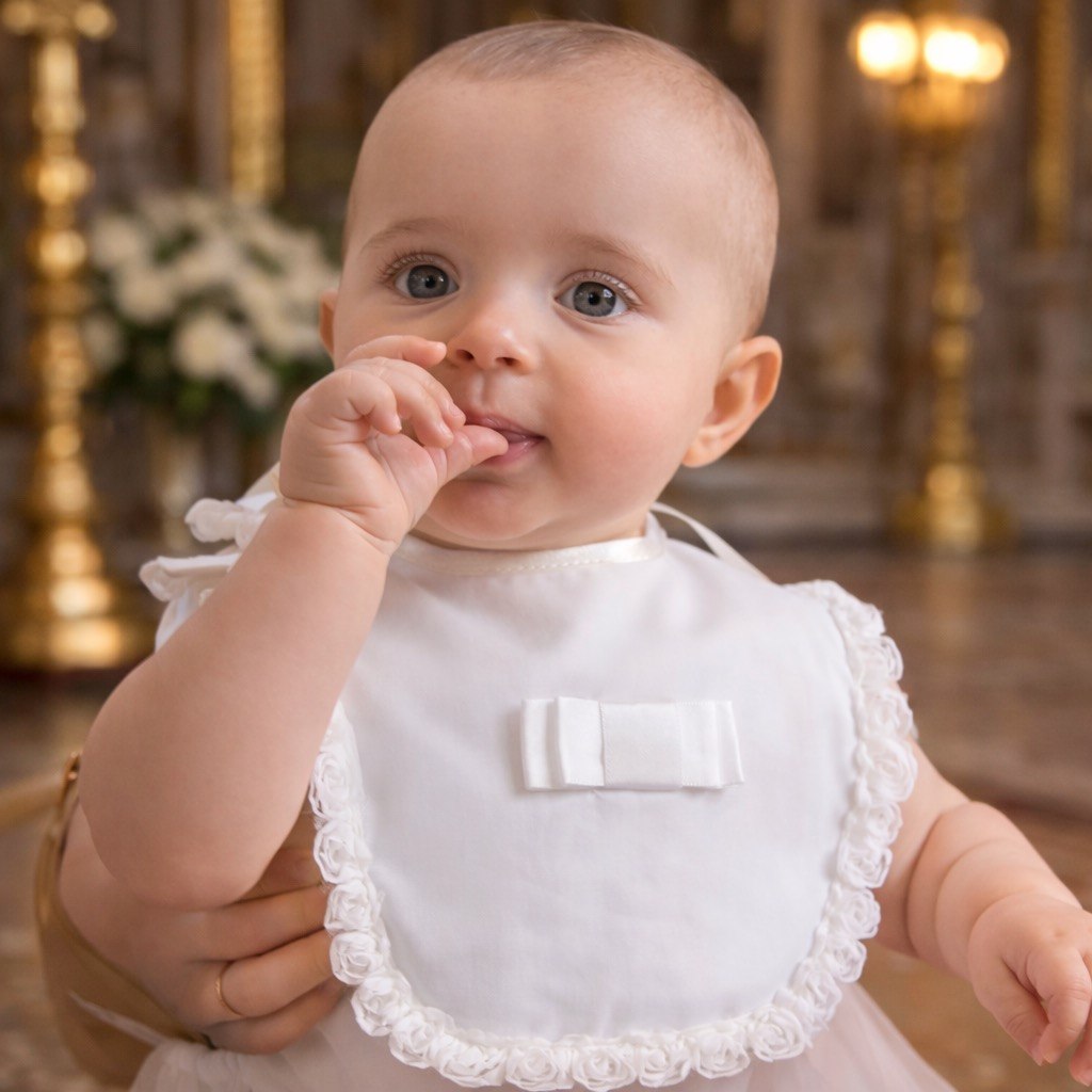 Baby wearing a white bib with lace trim in a decorated indoor setting