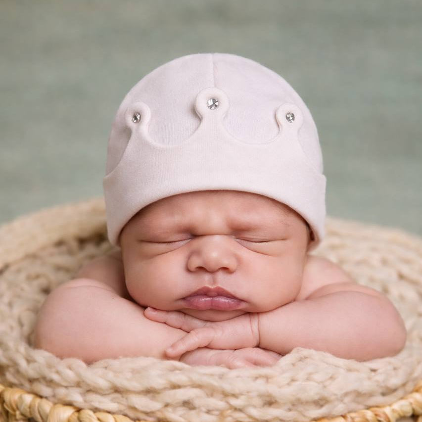 Newborn baby sleeping in a woven basket wearing a pink hat with decorative elements.