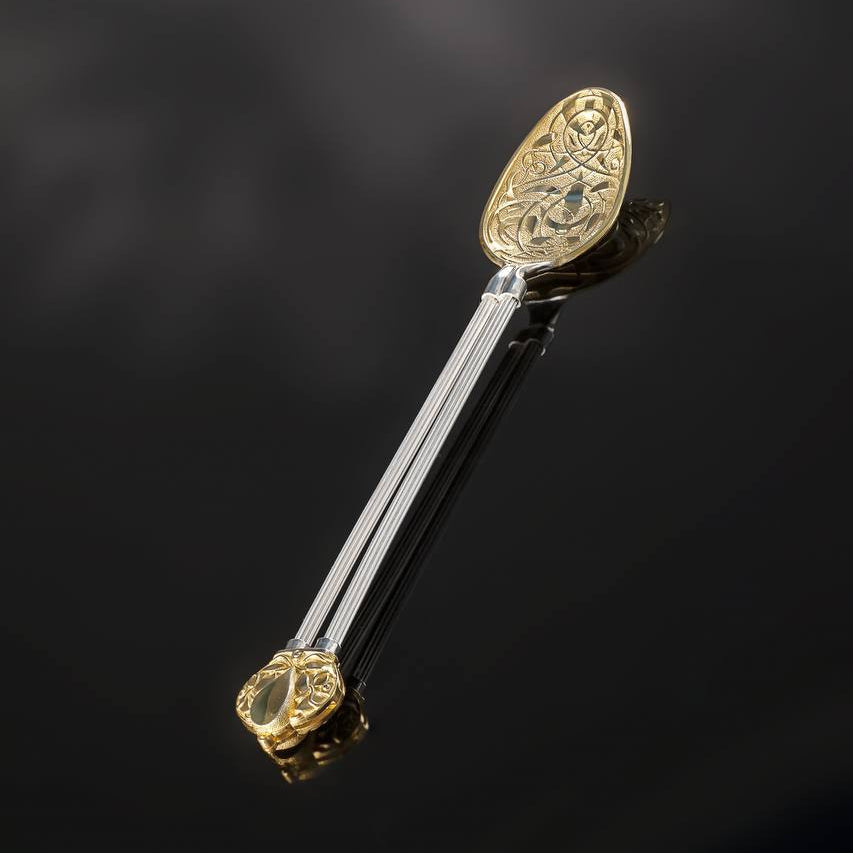 Decorative spoon with gold and silver design on a dark background