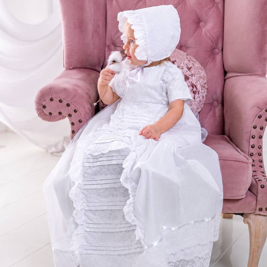 Child in a white lace dress sitting on a pink chair