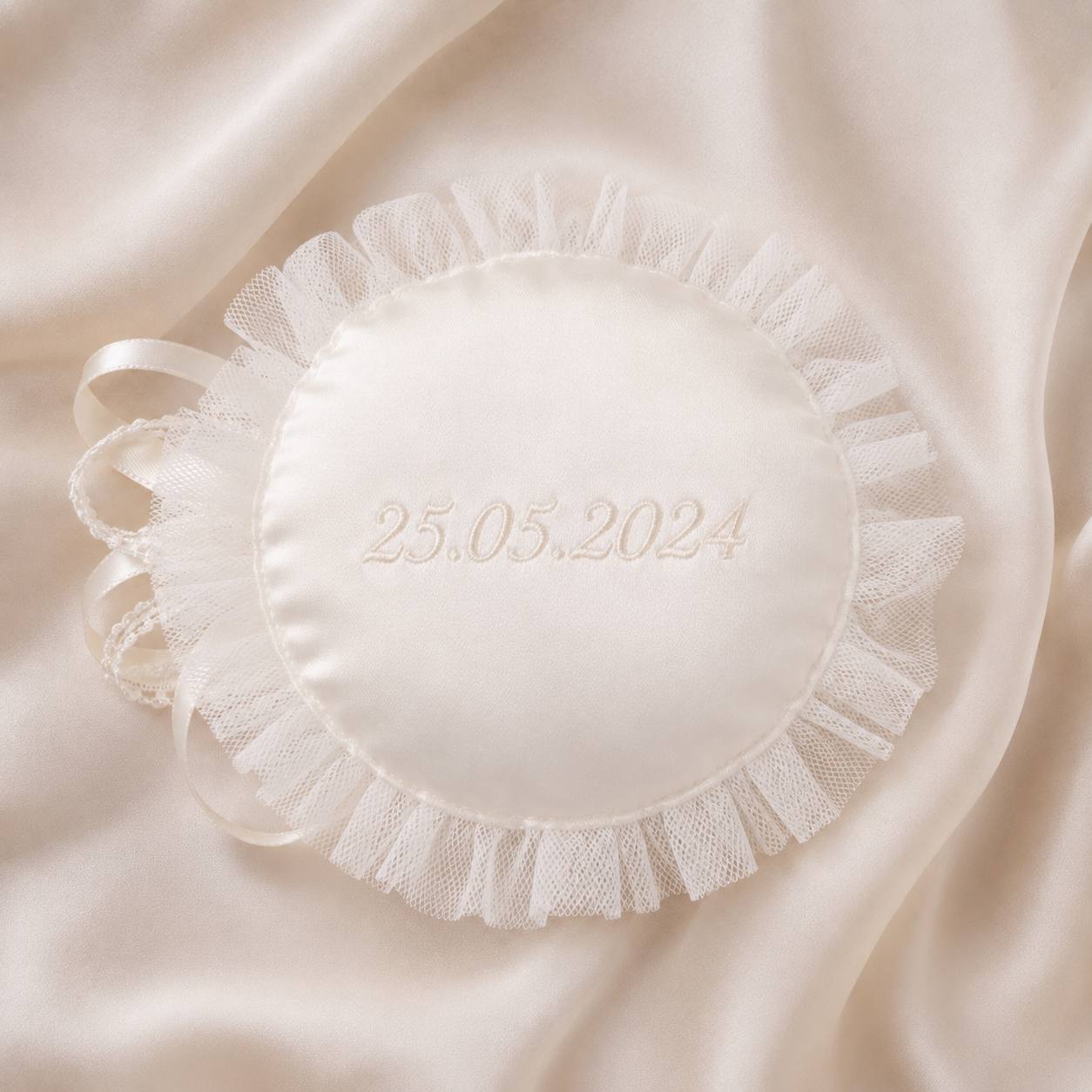 A round white satin keepsake pillow with a ruffled tassel and lace trim, featuring the date '25.05.
