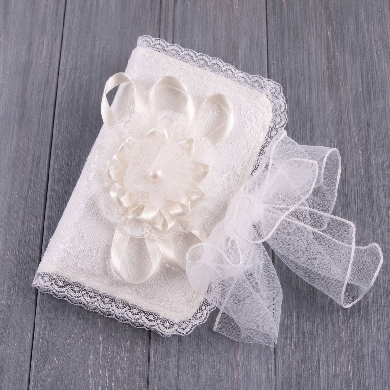 An ivory lace-covered Baby First Curl Keepsake Box or keepsake cover with a large fabric flower and pearl center, ribbon loops, and sheer tulle ties, photographed on a gray wood plank surface.