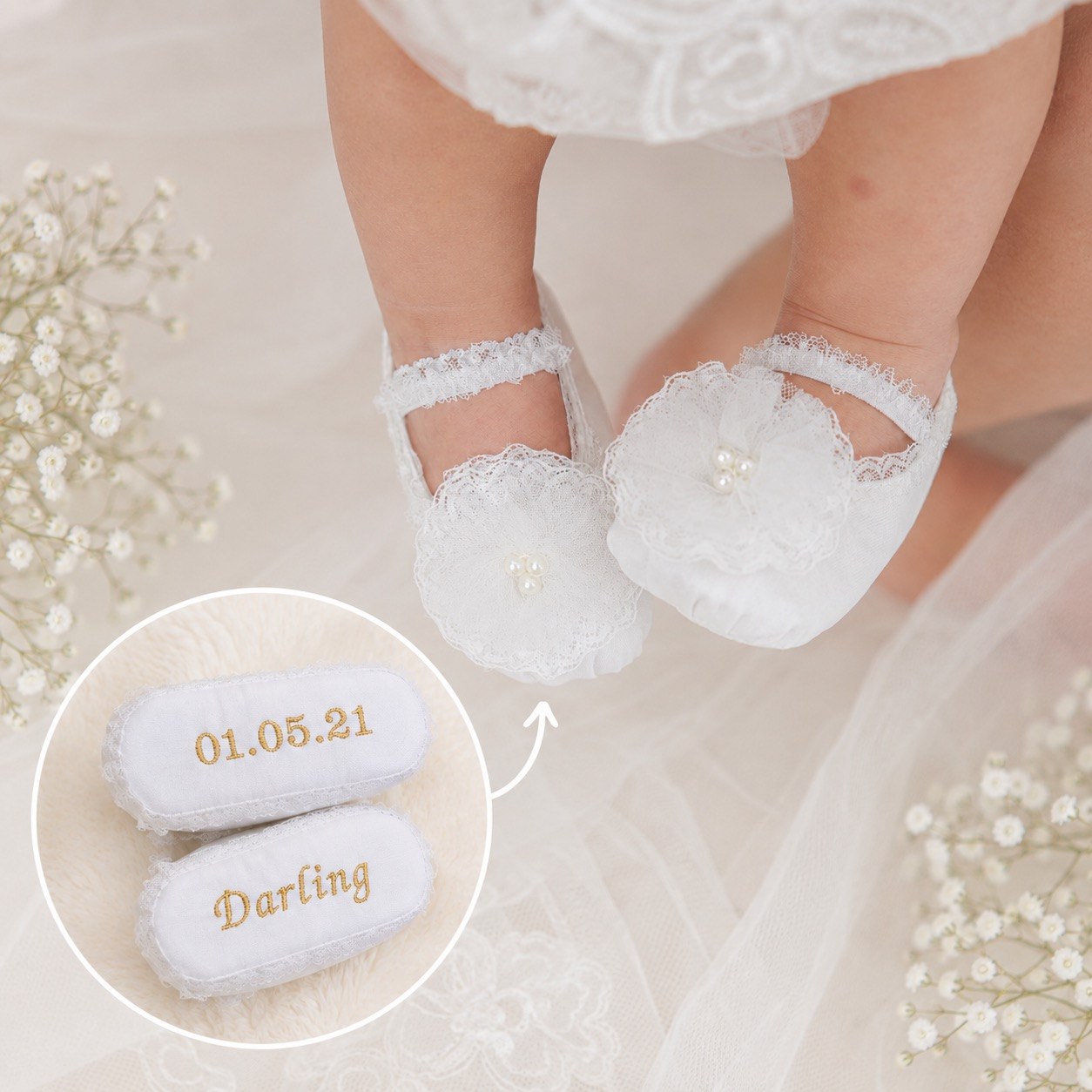 White lace baby booties with floral appliques and pearl details, shown on a baby's feet. A circular inset shows a pair of matching booties personalized with gold text reading '01.