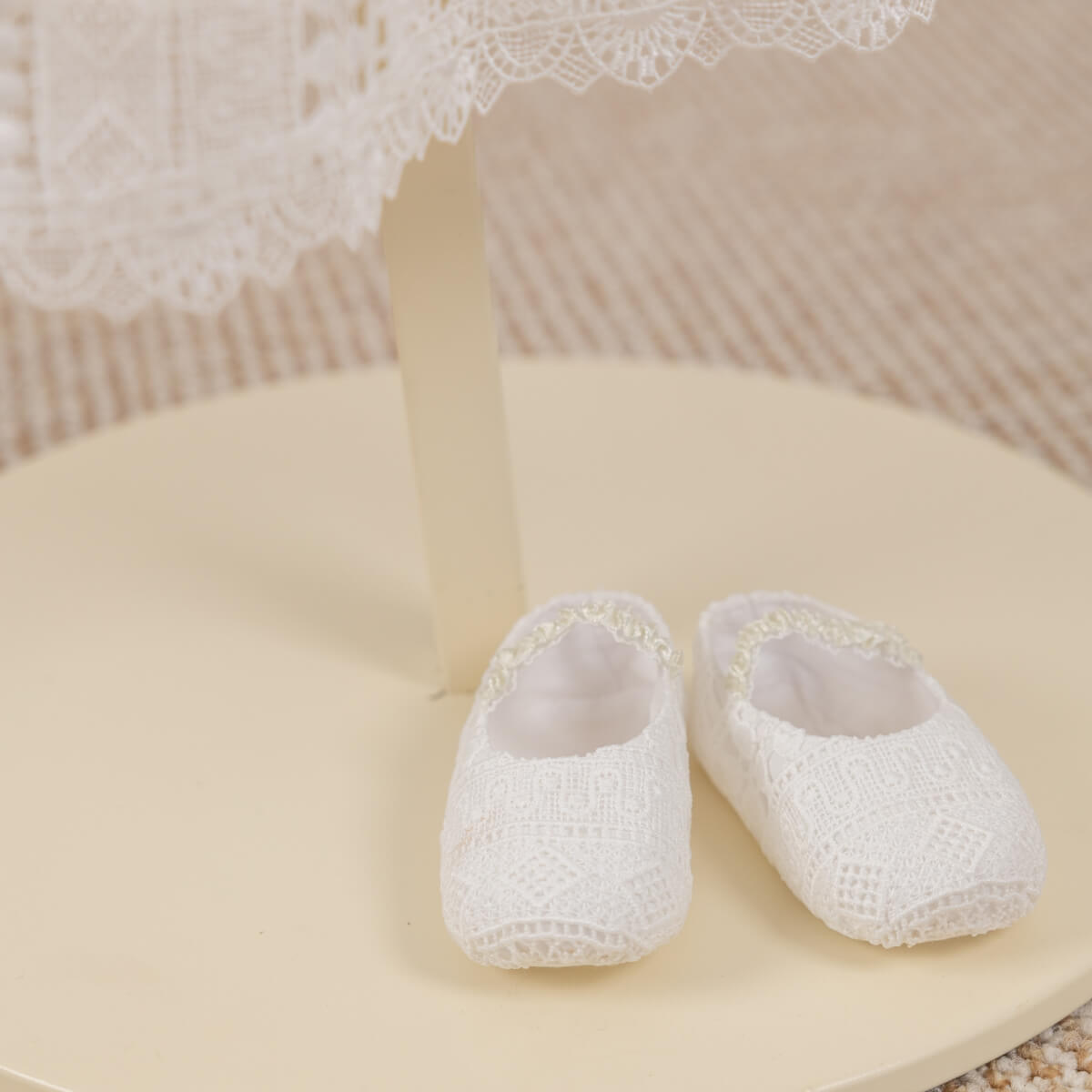 White baby booties on a light surface with lace in the background