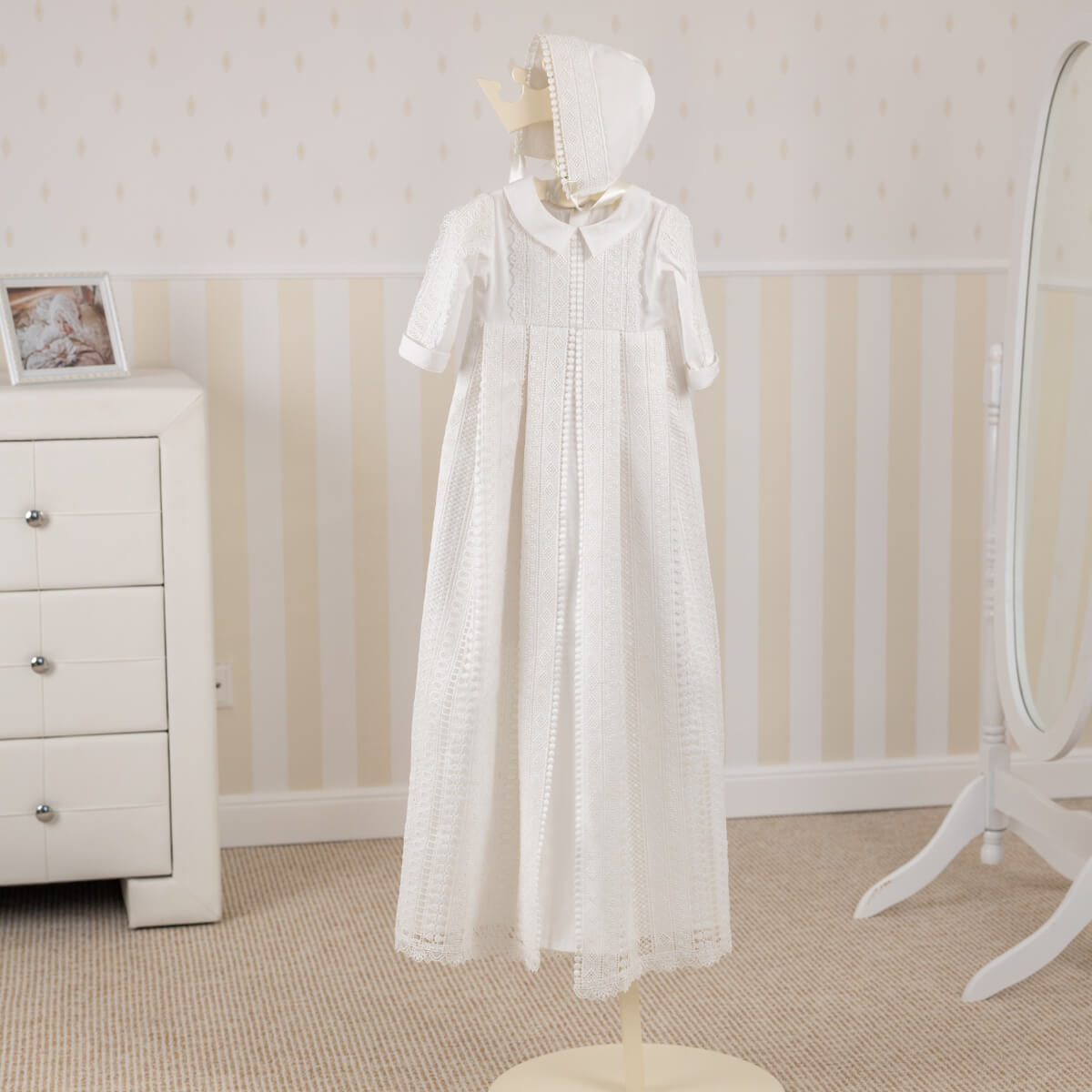Long lace christening gown on a mannequin in a nursery setting