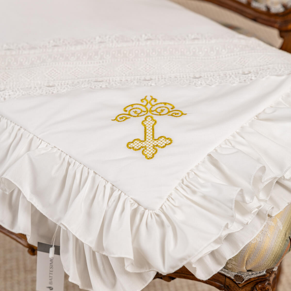 White embroidered cross on a white christening blanket with ruffled edges.