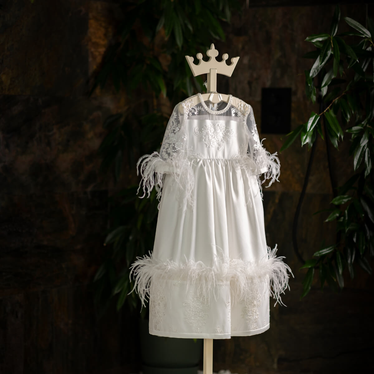 White lace Luxury Communion Dress with feather details on a mannequin against a dark background