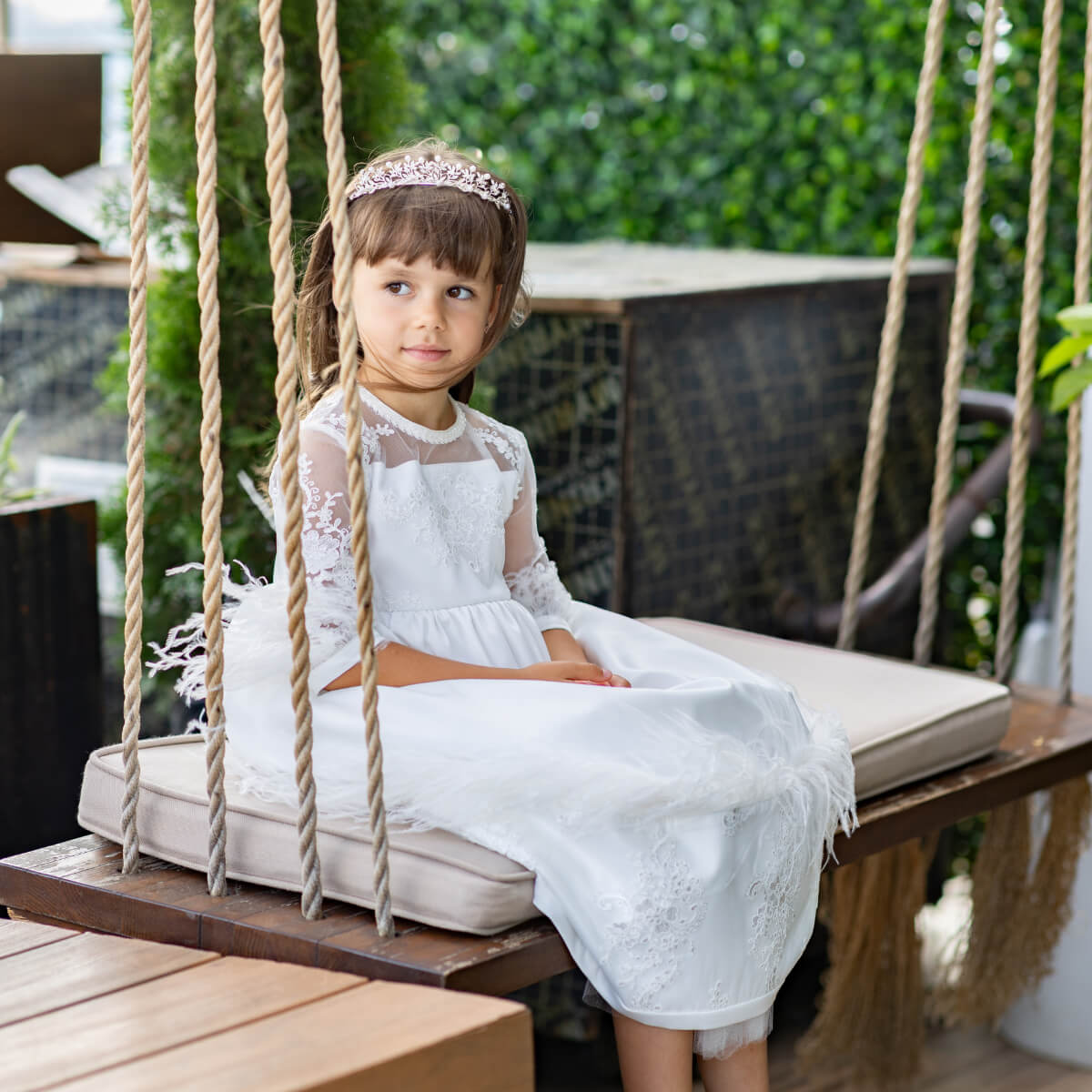 Young girl in a Luxury Communion Dress sitting on a swing outdoors.